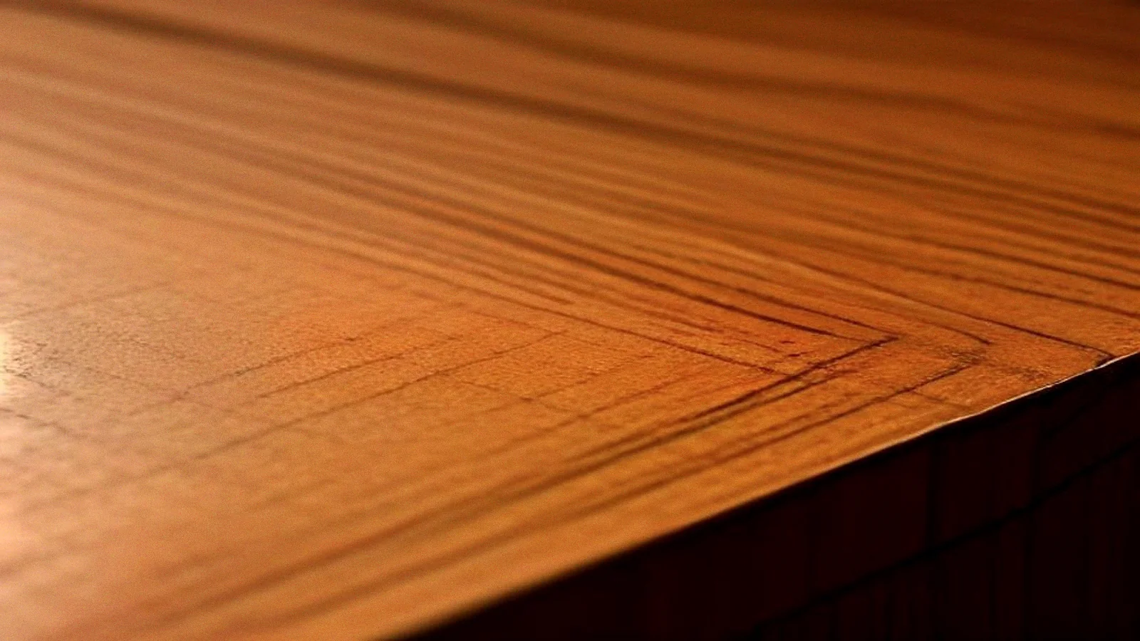 A close-up along the edge of a teak tabletop, the top surface turning over a worked bevel into the side.