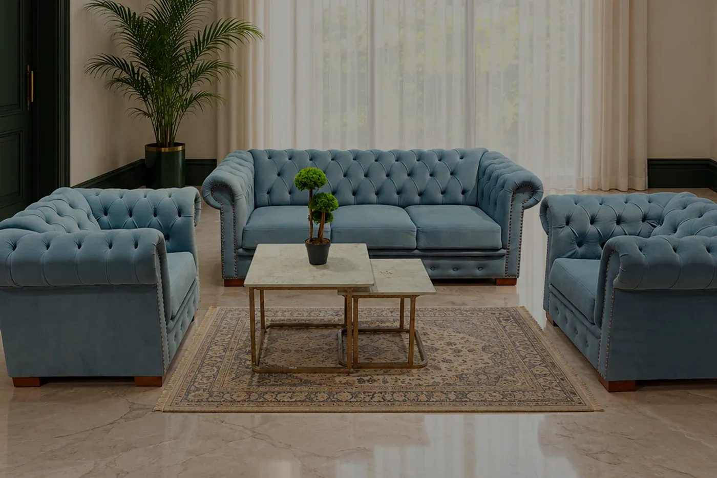 A powder-blue deep-buttoned sofa and two armchairs in a tall room with sheer curtains and a pale marble floor.