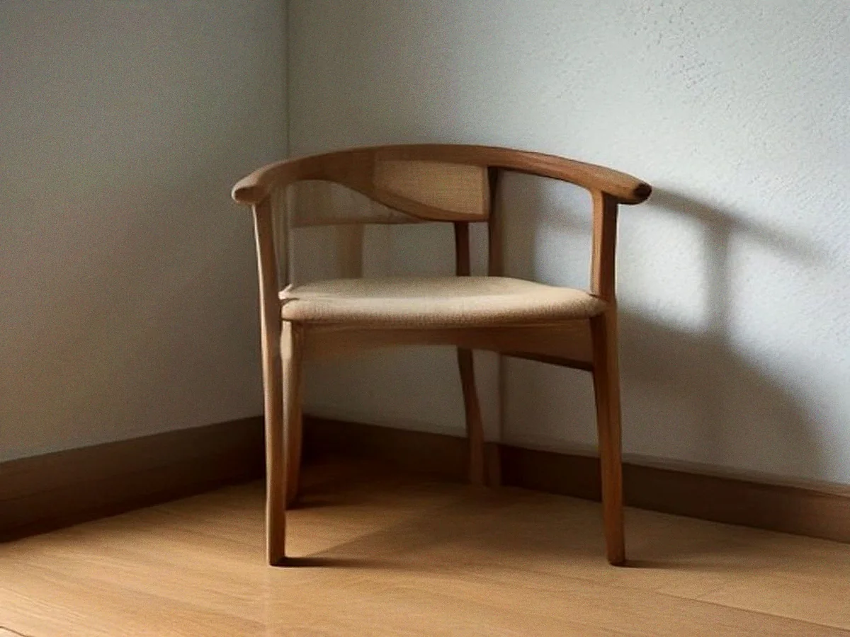 A teak armchair with a curved back rail and a pale seat, seen three-quarters on in raking light.