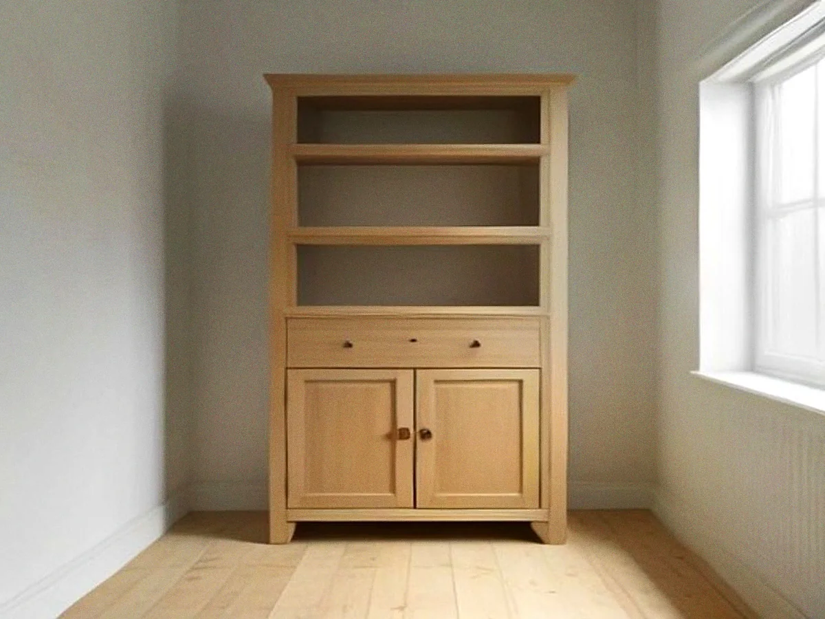 An unfinished cabinet in bare pale timber standing against a plain wall, open shelves above and two plain doors below, no polish on it yet.